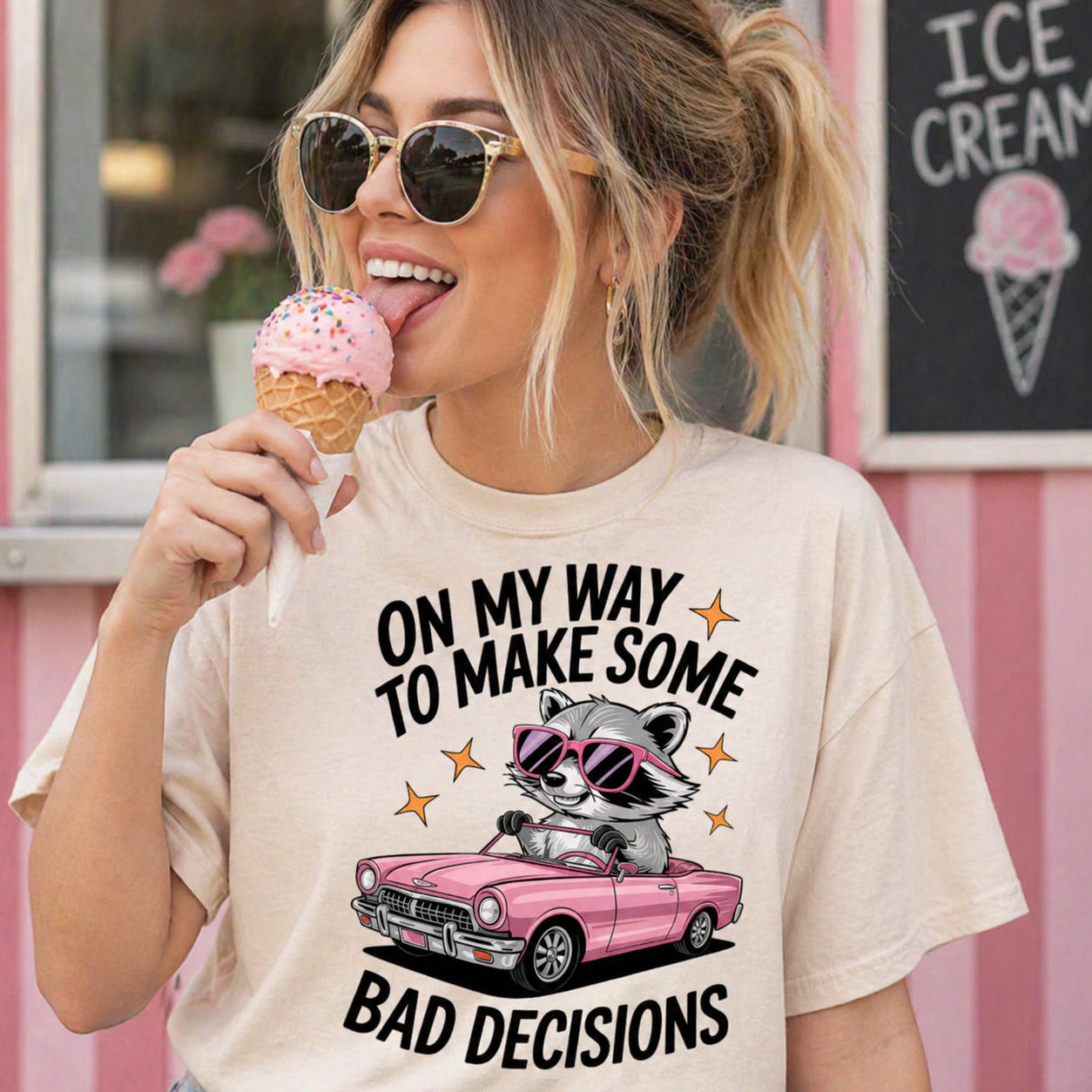 Woman wearing an ivory colored t-shirt with a raccoon graphic and text, eating ice cream in front of an ice cream shop.