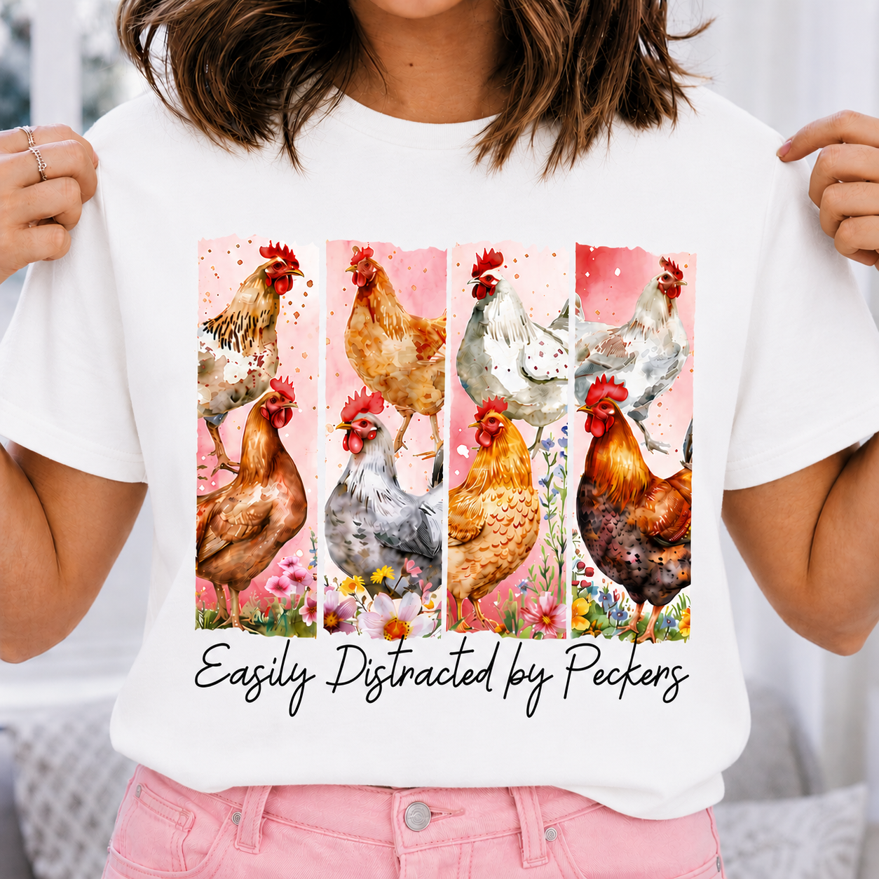 White colored t-shirt with chicken design and text 'Easily Distracted by Peckers' held by a person.
