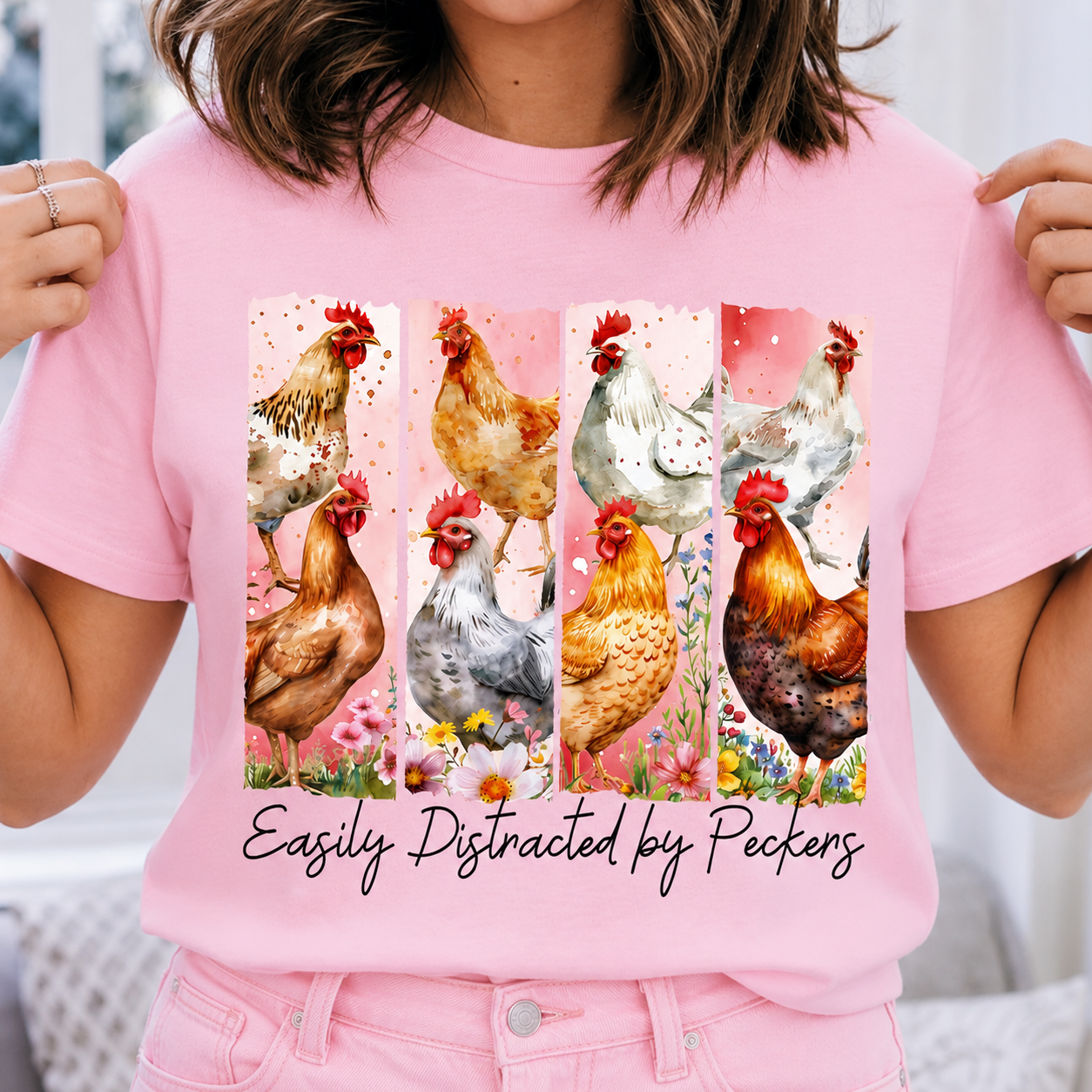 Blossom colored t-shirt with chicken design and text 'Easily Distracted by Peckers' held by a person.