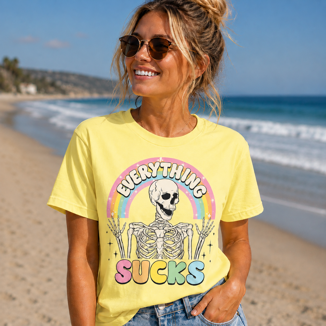 Woman wearing a yellow t-shirt with a skeleton graphic and text on a beach.