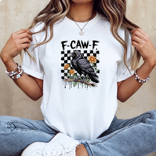 A woman wearing a white graphic t-shirt with a black raven and the text 'F-CAW-F' on a checkered background, paired with blue jeans and white sneakers.