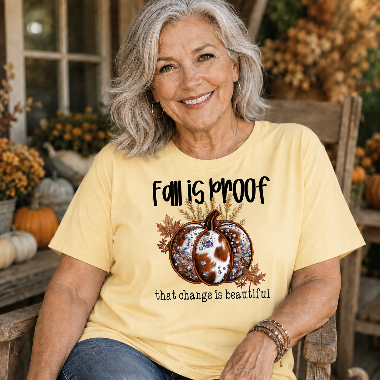 Woman wearing a butter colored t-shirt  with the phrase “Fall Is Proof That Change Is Beautiful” in faux-embroidery style.