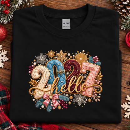 A folded black Gildan t-shirt with a colorful '2027 hello' graphic on the front, styled on a rustic wooden background with Christmas decorations.