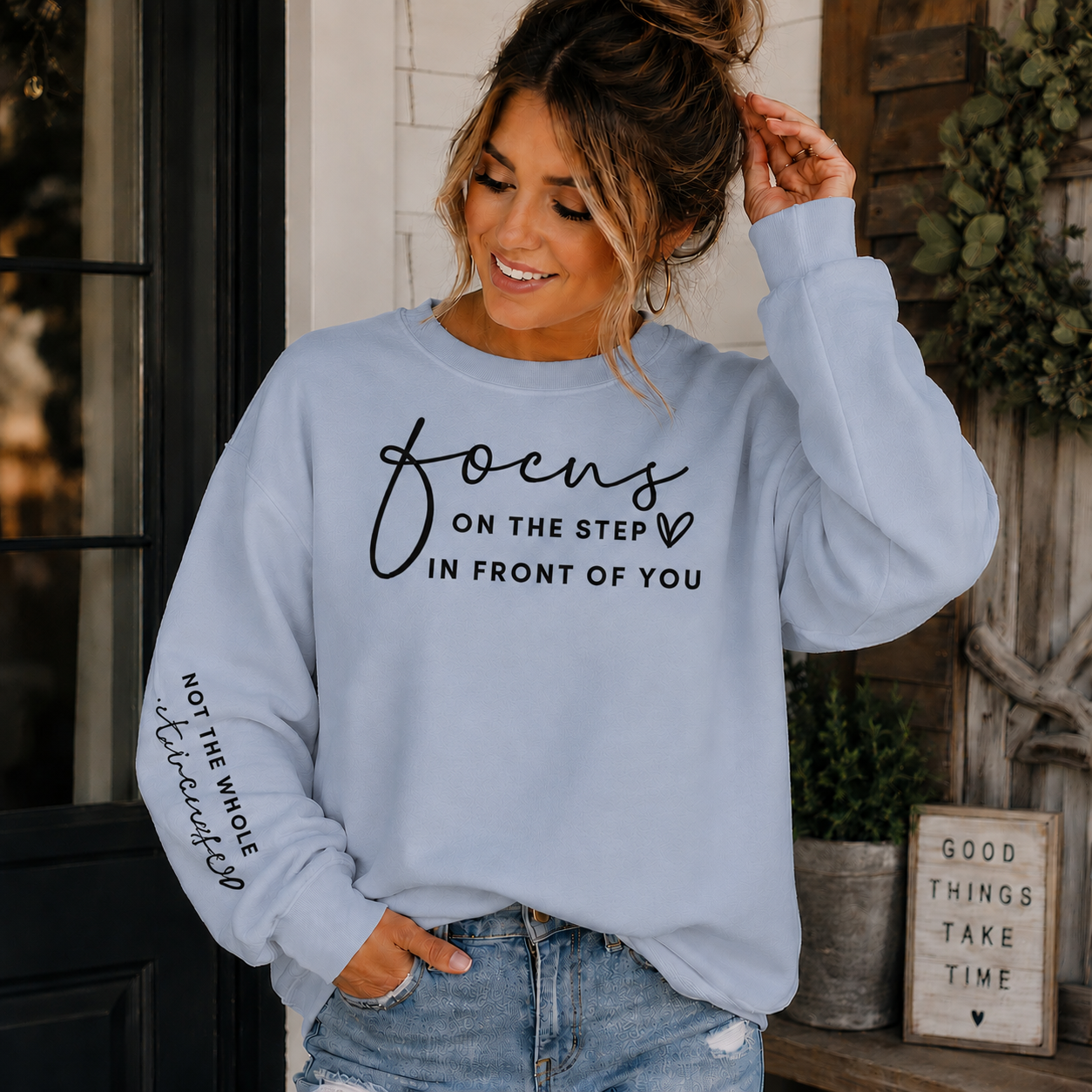 Woman wearing a light blue sweatshirt with black text Focus on the step in front of you not the whole staircase