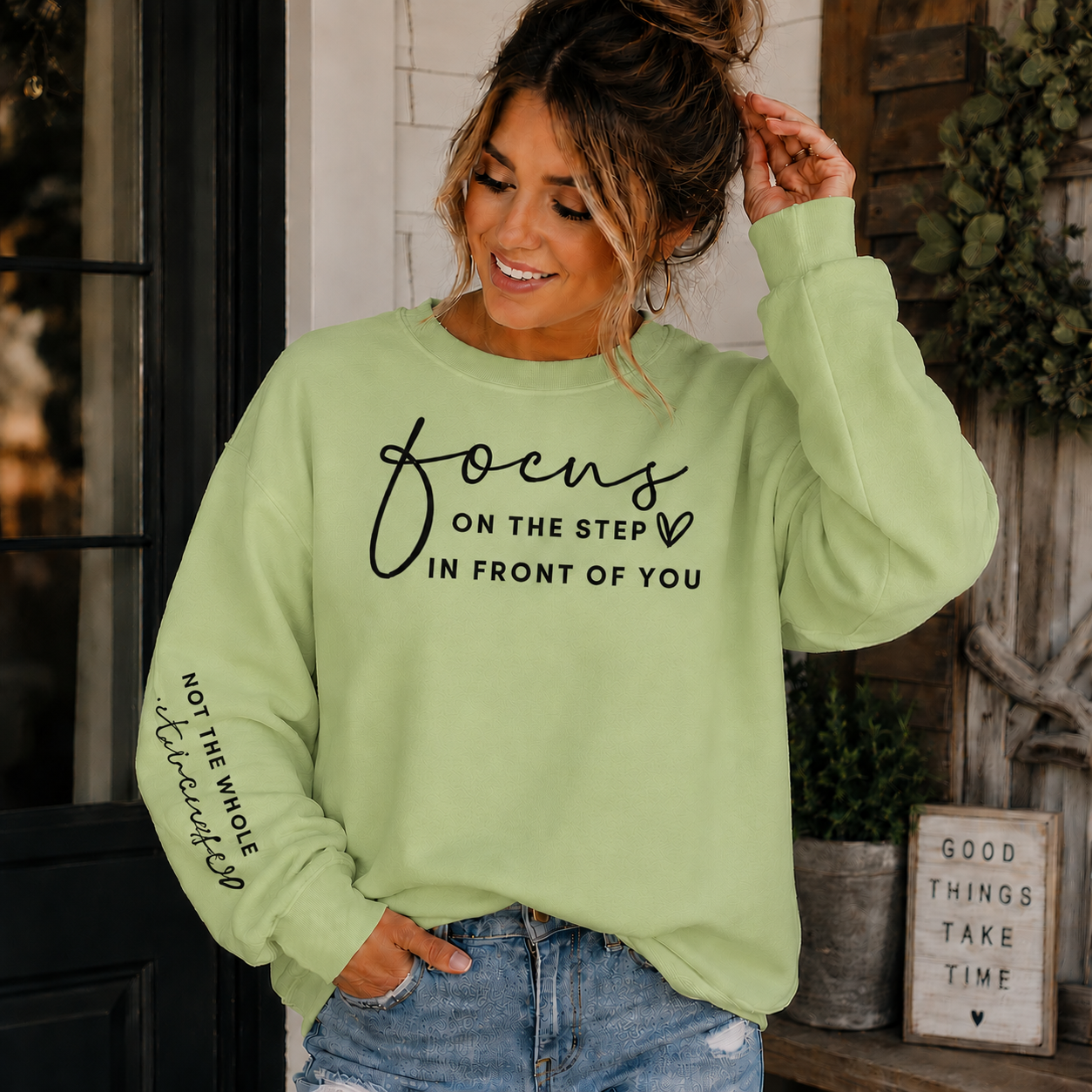 Woman wearing a pistachio colored  sweatshirt with black text Focus on the step in front of you not the whole staircase