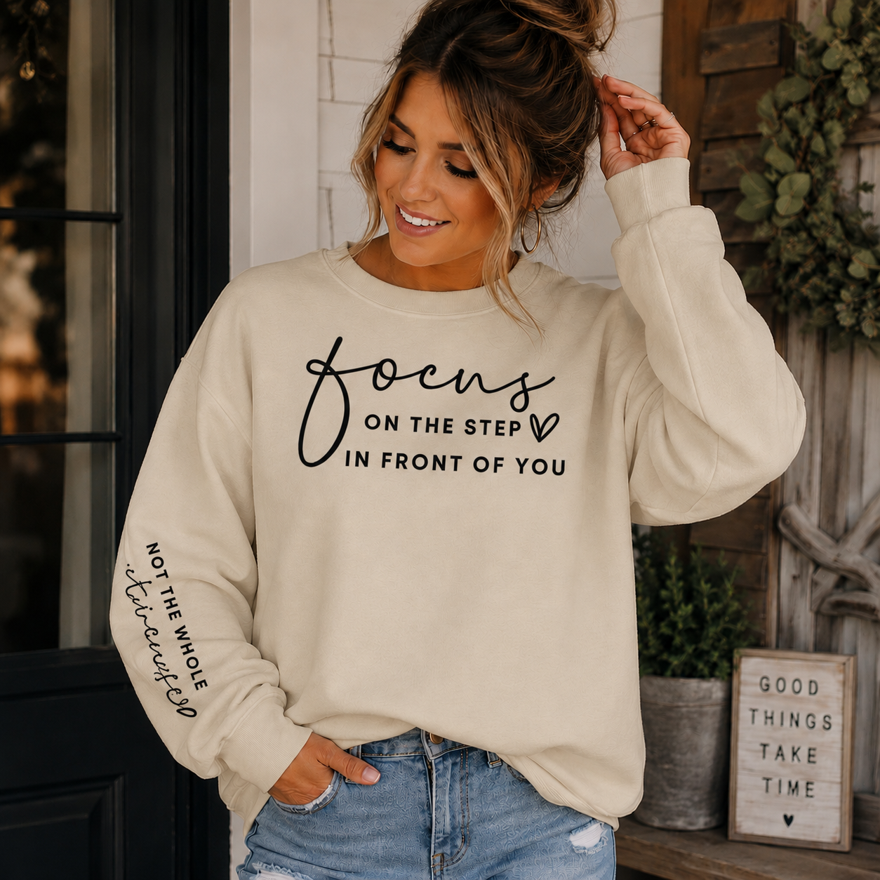 Woman wearing a sand sweatshirt with black text Focus on the step in front of you not the whole staircase