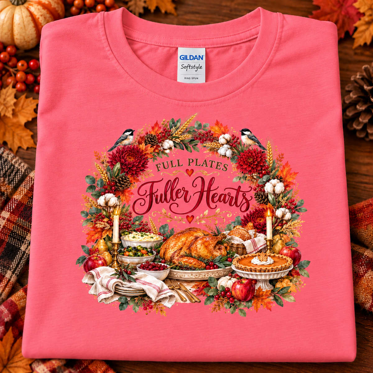 A folded coral pink Gildan Softstyle t-shirt with a detailed autumn Thanksgiving graphic, displayed on a rustic wooden background with fall leaves and pinecones.
