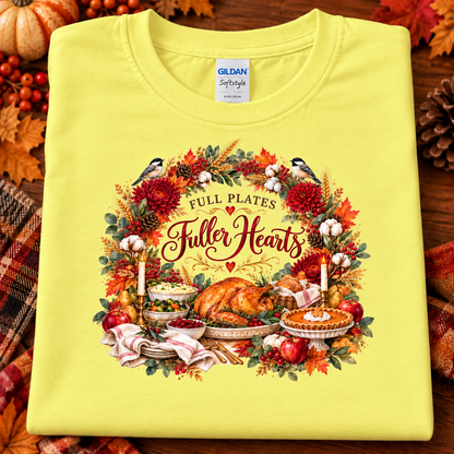 A folded cornsilk yellow Gildan Softstyle T-shirt with a large Thanksgiving-themed graphic print reading 'Full Plates Fuller Hearts,' featuring a roasted turkey, pie, candles, berries, autumn leaves, and birds. The shirt is styled on a wooden surface with fall decor around itsilk