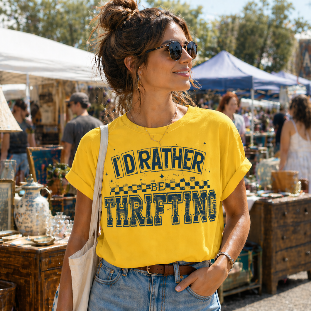 Woman wearing a yellow t-shirt with 'I'd Rather Be Thrifting' text at an outdoor market.