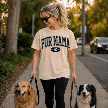 Woman walking two dogs on a sidewalk wearing a natural colored t-shirt with 'FUR MAMA' Text.