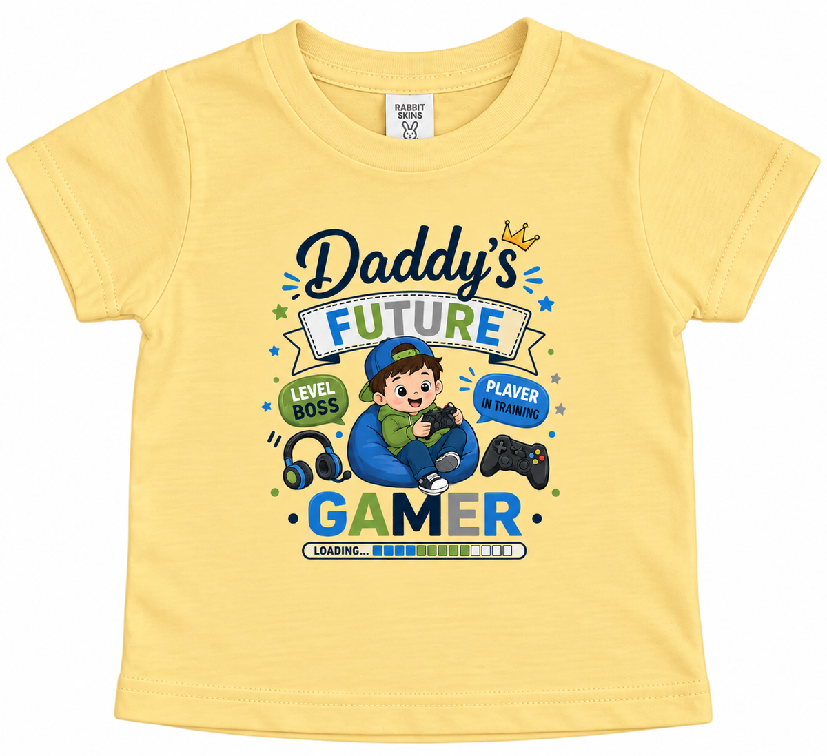 A butter yellow short-sleeve baby t-shirt with a colorful graphic print on the front. The graphic reads 'Daddy's FUTURE GAMER' with a cartoon boy sitting in a blue bean bag, wearing a cap and holding a controller, surrounded by game-themed icons like headphones, a controller, and a crown.