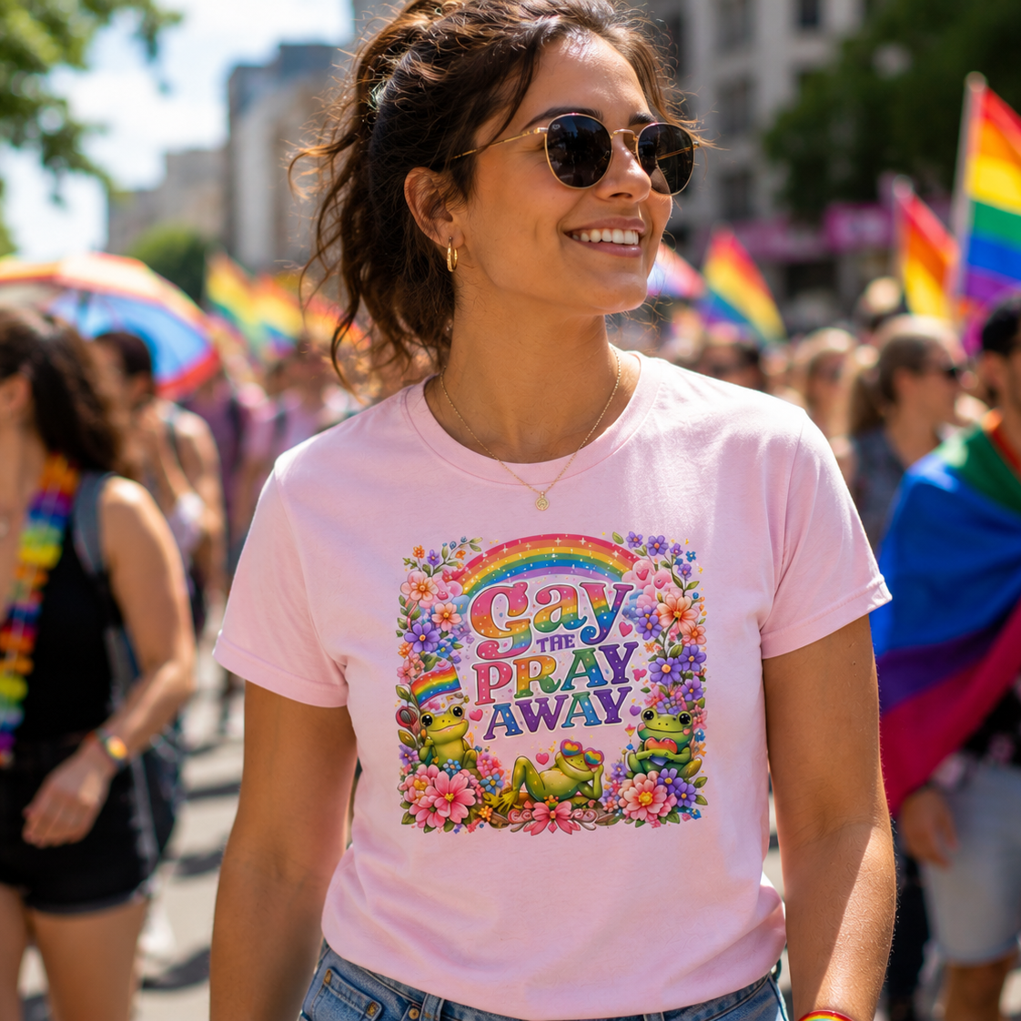 Woman wearing a light pink Gay The Pray Away pride graphic t-shirt with rainbow frogs and flowers at a Pride parade.