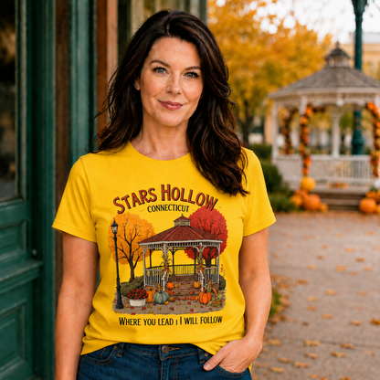 Woman wearing a 'Stars Hollow Connecticut' daisycolored t-shirt with a scenic design in an outdoor setting.