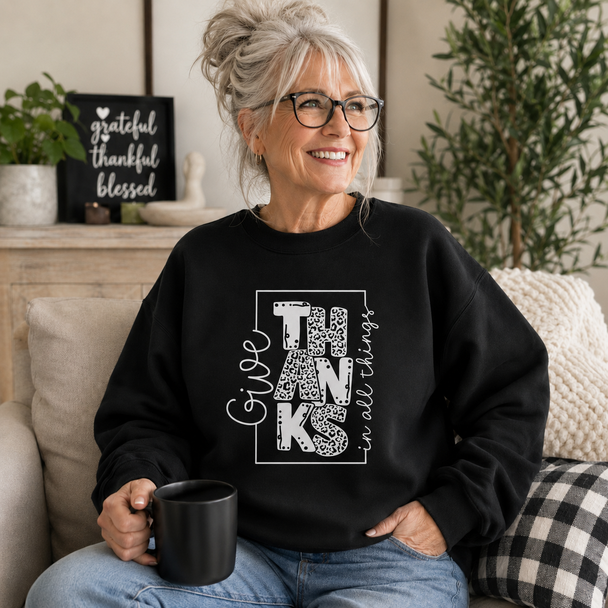 Woman wearing a black colored sweatshirt with text “Give Thanks in All Things” soft, comfy, and perfect for Thanksgiving or everyday fall wear.