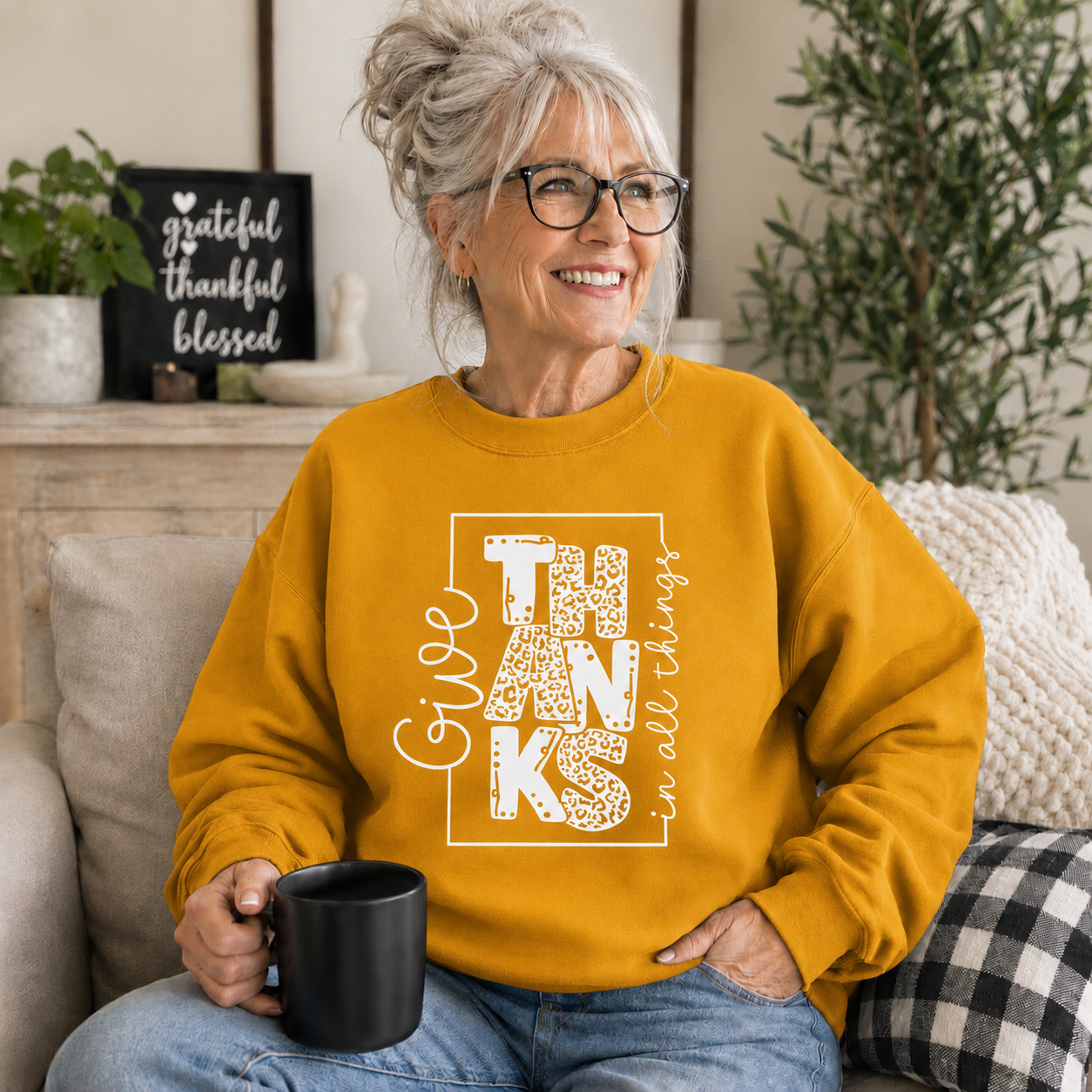 Woman wearing a gold colored sweatshirt with text “Give Thanks in All Things” soft, comfy, and perfect for Thanksgiving or everyday fall wear.