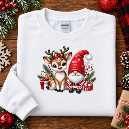 A white long-sleeve crewneck sweatshirt with a Christmas graphic of a reindeer and gnome, laid flat on a wooden surface with holiday decorations.
