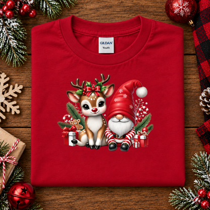 A folded red Gildan Youth t-shirt with a Christmas graphic of a reindeer and Santa Claus, displayed on a wooden background with holiday decorations.