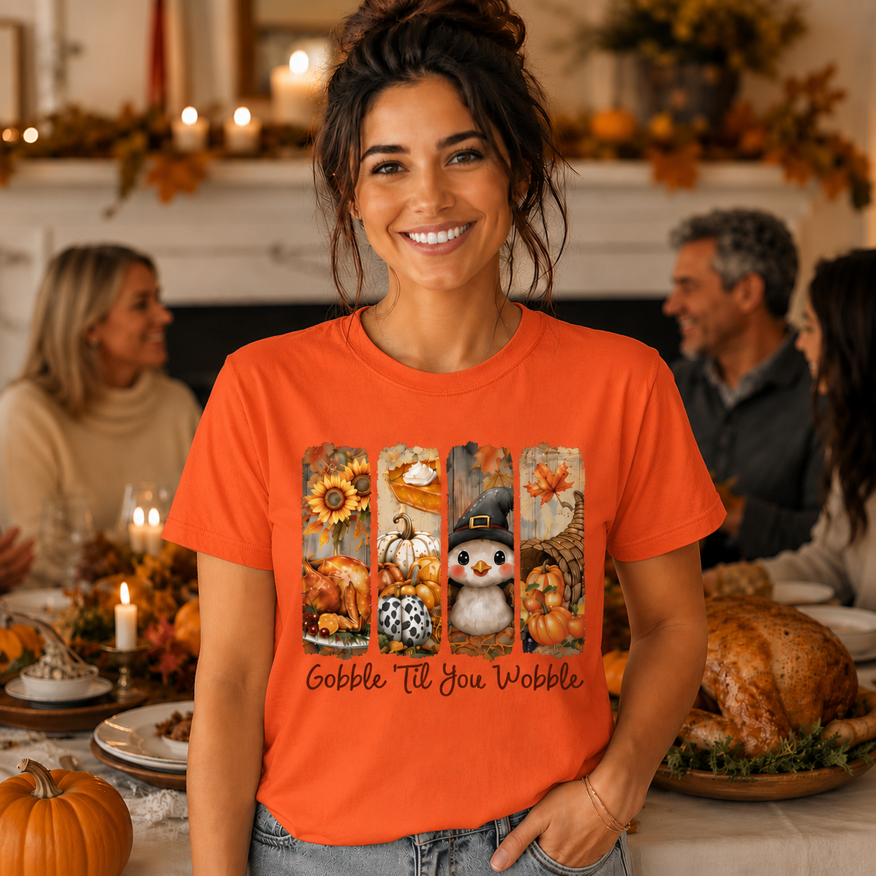 A smiling woman stands in a warmly lit dining room wearing an orange graphic T-shirt with autumn-themed illustrations and the text 'Gobble Till You Wobble.' The background shows a Thanksgiving table with candles, plates, and a roasted turkey.