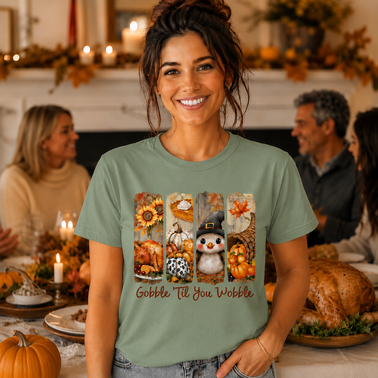 A woman wearing a sage green graphic t-shirt with a fall-themed 'Gobble Till You Wobble' design, standing in a cozy, warmly lit Thanksgiving dining room with family and a roasted turkey in the background.