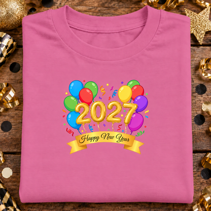 A folded azalea pink t-shirt features a colorful graphic of balloons, gold 3D numbers spelling '2027', and a gold banner reading 'Happy New Year'.