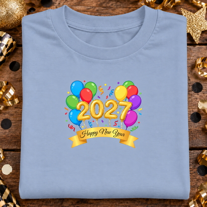 A folded light blue t-shirt features a colorful graphic of balloons, gold 3D numbers spelling '2027', and a gold banner reading 'Happy New Year'.
