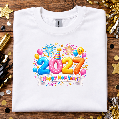 A folded white Gildan t-shirt with a colorful '2027 Happy New Year!' graphic, displayed on a wooden surface surrounded by gold and black party decorations.