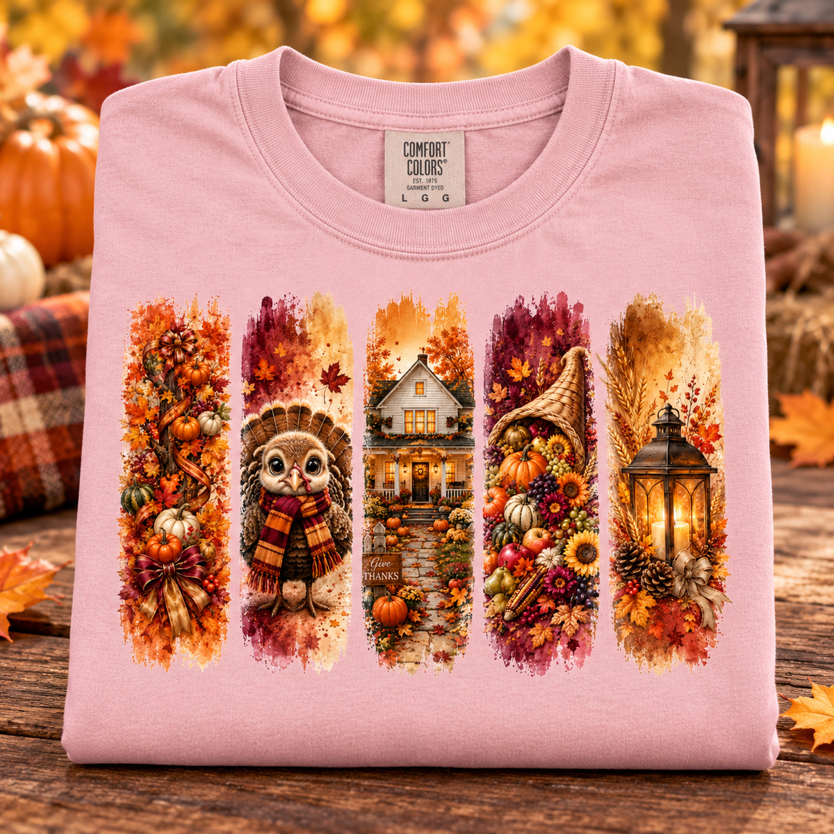 A folded blossom pink Comfort Colors t-shirt with a detailed autumn-themed graphic print, displayed on a rustic wooden surface with fall decorations in the background.