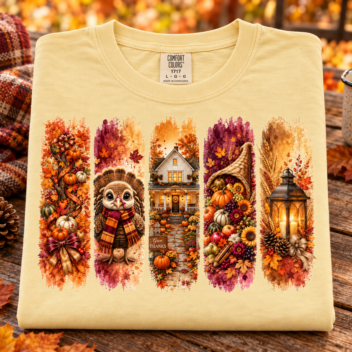 A folded butter colored Comfort Colors t-shirt with a detailed autumn Thanksgiving graphic print, displayed on a rustic wooden table with scattered fall leaves.