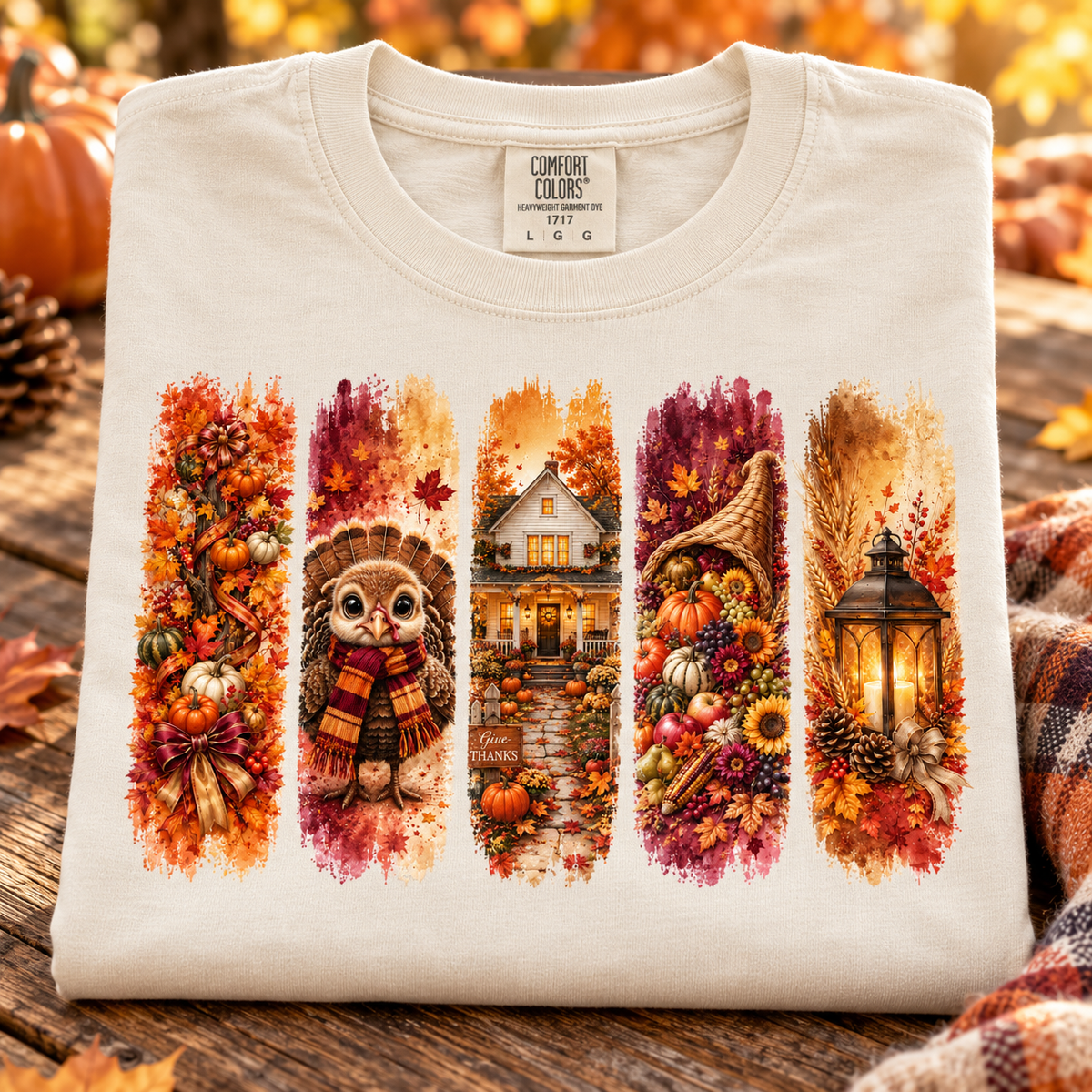 A folded ivory colored Comfort Colors t-shirt with a detailed autumn-themed graphic print, displayed on a rustic wooden surface with a plaid blanket and pumpkins in the background.