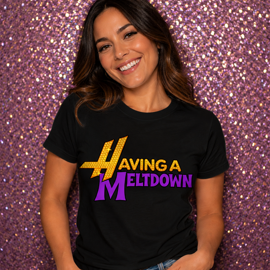 Woman wearing a black graphic t-shirt with colorful retro “Having A Meltdown” design standing in front of a pink glittery wall.