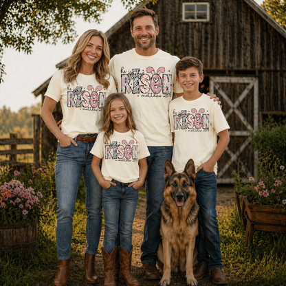 Family of four wearing a He is risen graphic t-shirt with a dog standing in front of a wooden barn.
