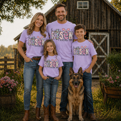 Family of four wearing a He is risen graphic t-shirt on Orchid with a dog standing in front of a wooden barn.