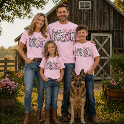 Family of four wearing a He is risen graphic t-shirt on blossom with a dog standing in front of a wooden barn.