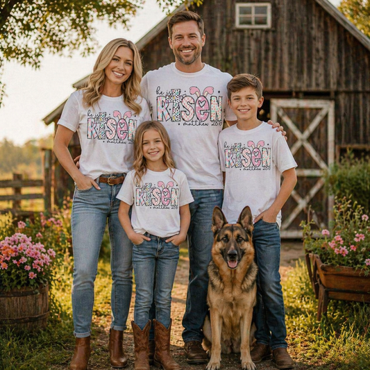 Family of four wearing a He is risen graphic t-shirt on white with a dog standing in front of a wooden barn.