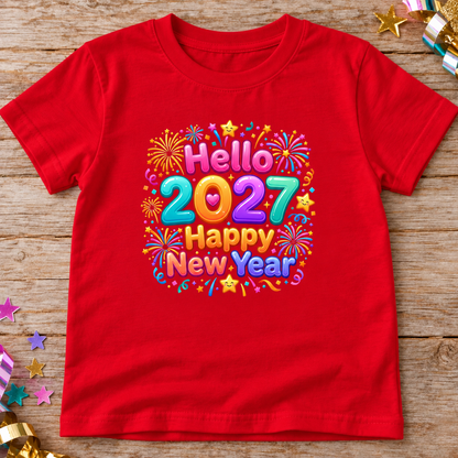 A red short-sleeve t-shirt laid flat on a rustic wooden surface, featuring a colorful 'Hello 2027 Happy New Year' graphic with fireworks and stars. Decorative star and ribbon confetti is scattered around the edges.