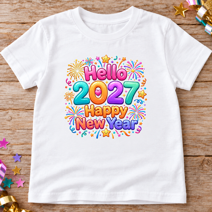 A white short-sleeve t-shirt laid flat on a rustic wooden surface, featuring a colorful 'Hello 2027 Happy New Year' graphic with fireworks, stars, and confetti.