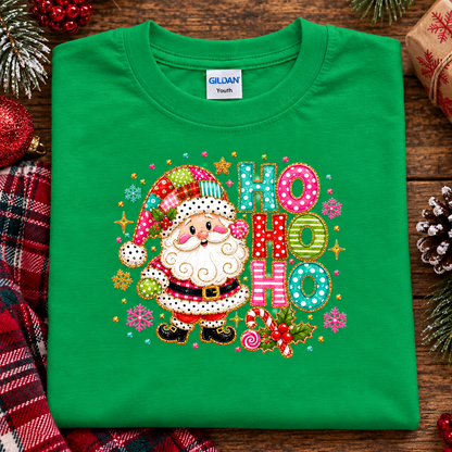A folded irish green Gildan Youth t-shirt featuring a colorful embroidered Christmas design with a Santa Claus character and 'HO HO HO' lettering, styled on a rustic wooden background with holiday decorations.