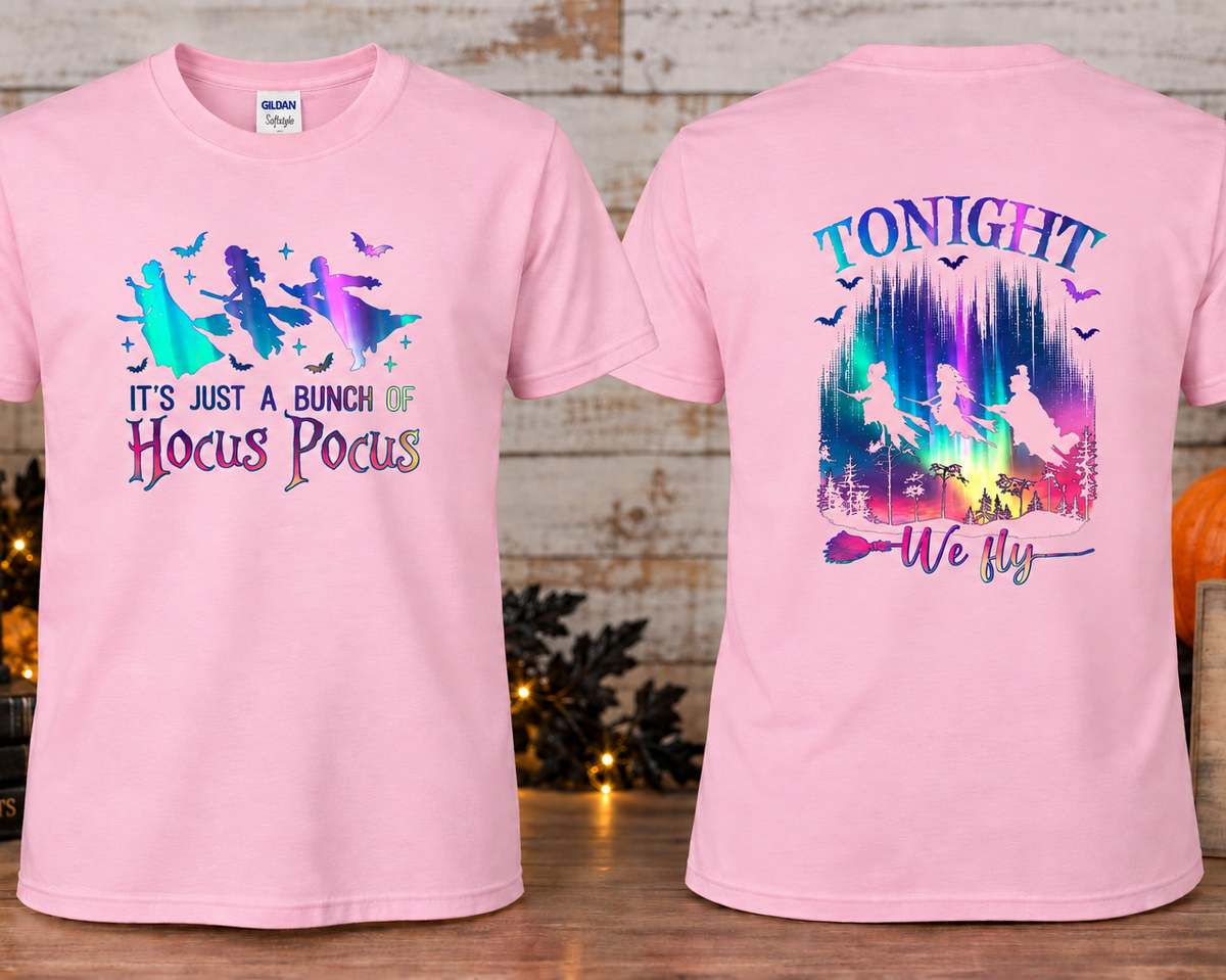 A light pink short-sleeve graphic T-shirts shown front and back on a styled tabletop setup. The front has a witch silhouette graphic with the text 'IT'S JUST A BUNCH OF Hocus Pocus.