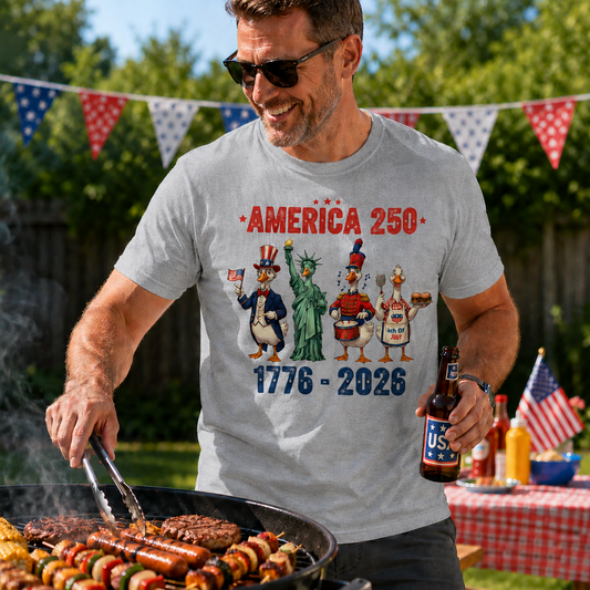 Man grilling outdoors wearing a sport gray t-shirt with 'America 250' design, surrounded by flags and food.