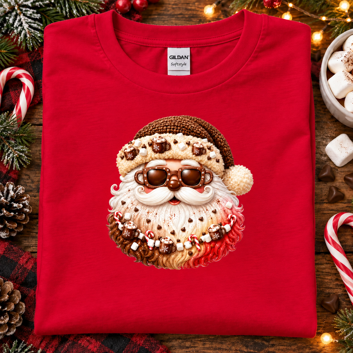A folded red Gildan Signature t-shirt featuring a festive Santa Claus face graphic made of candy canes, marshmallows, and chocolate, displayed on a rustic wooden background with Christmas decorations.