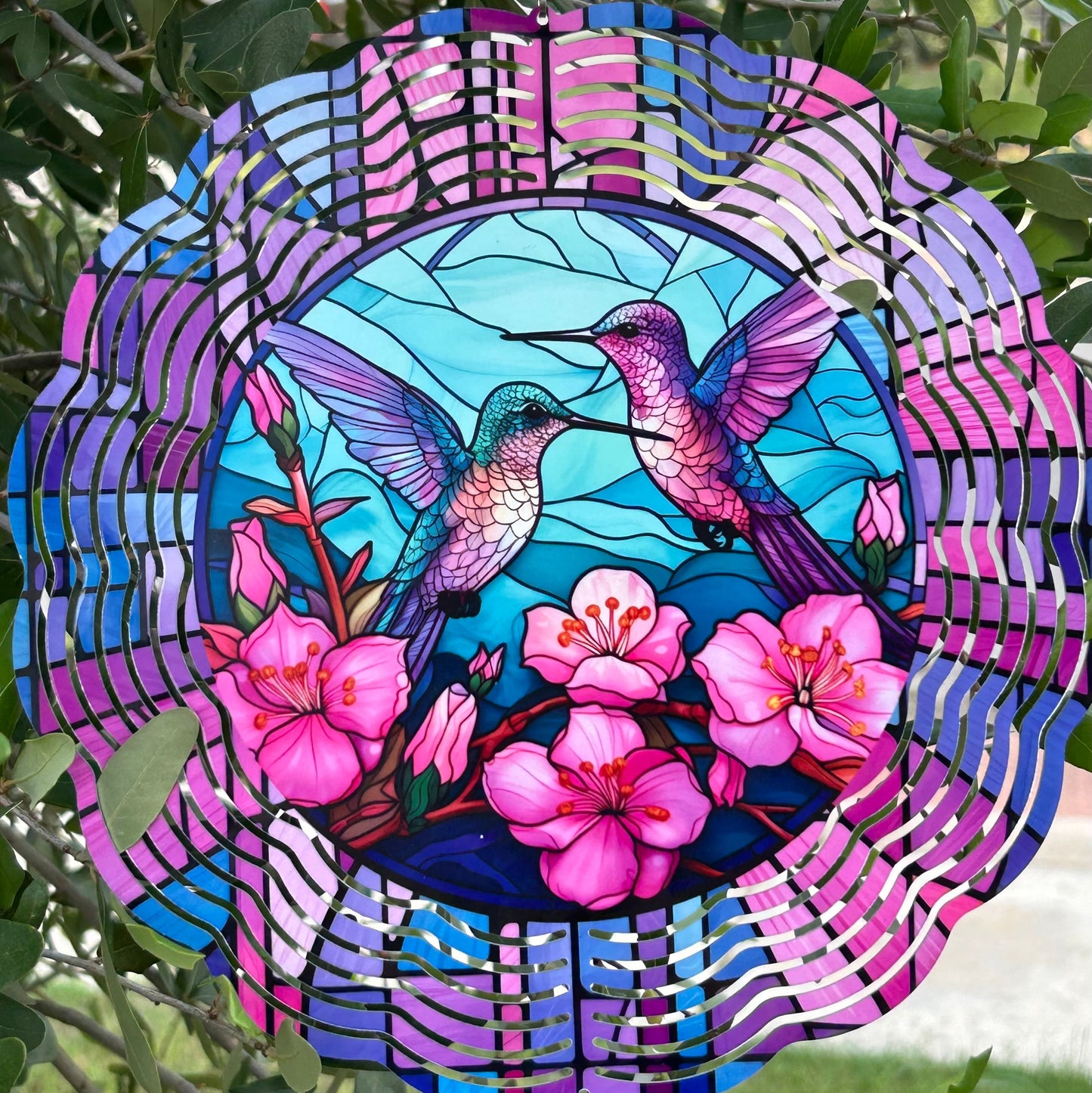 Wind spinner with hummingbirds and flowers, hanging among green leaves.