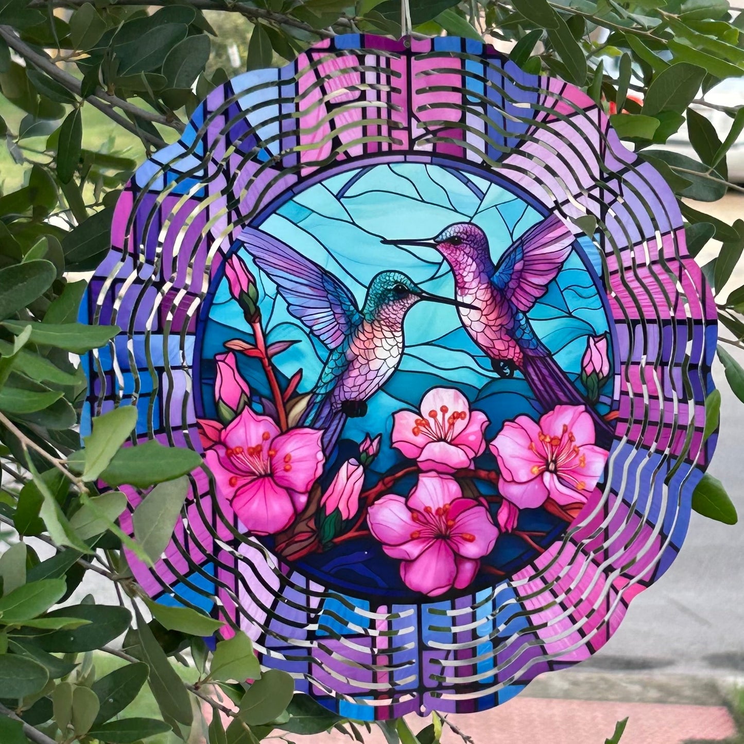 Wind spinner with hummingbirds and flowers hanging among green leaves.