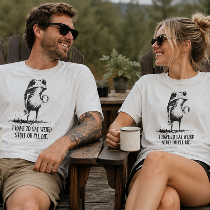 Two people sitting outdoors wearing matching white t-shirts with a graphic of a frog with humorous text