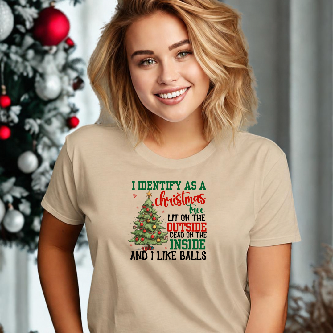 A woman wearing a sand colored t-shirt with a Christmas tree graphic with the words I identify as a Christmas tree lit on the outside dead on the inside and I like balls