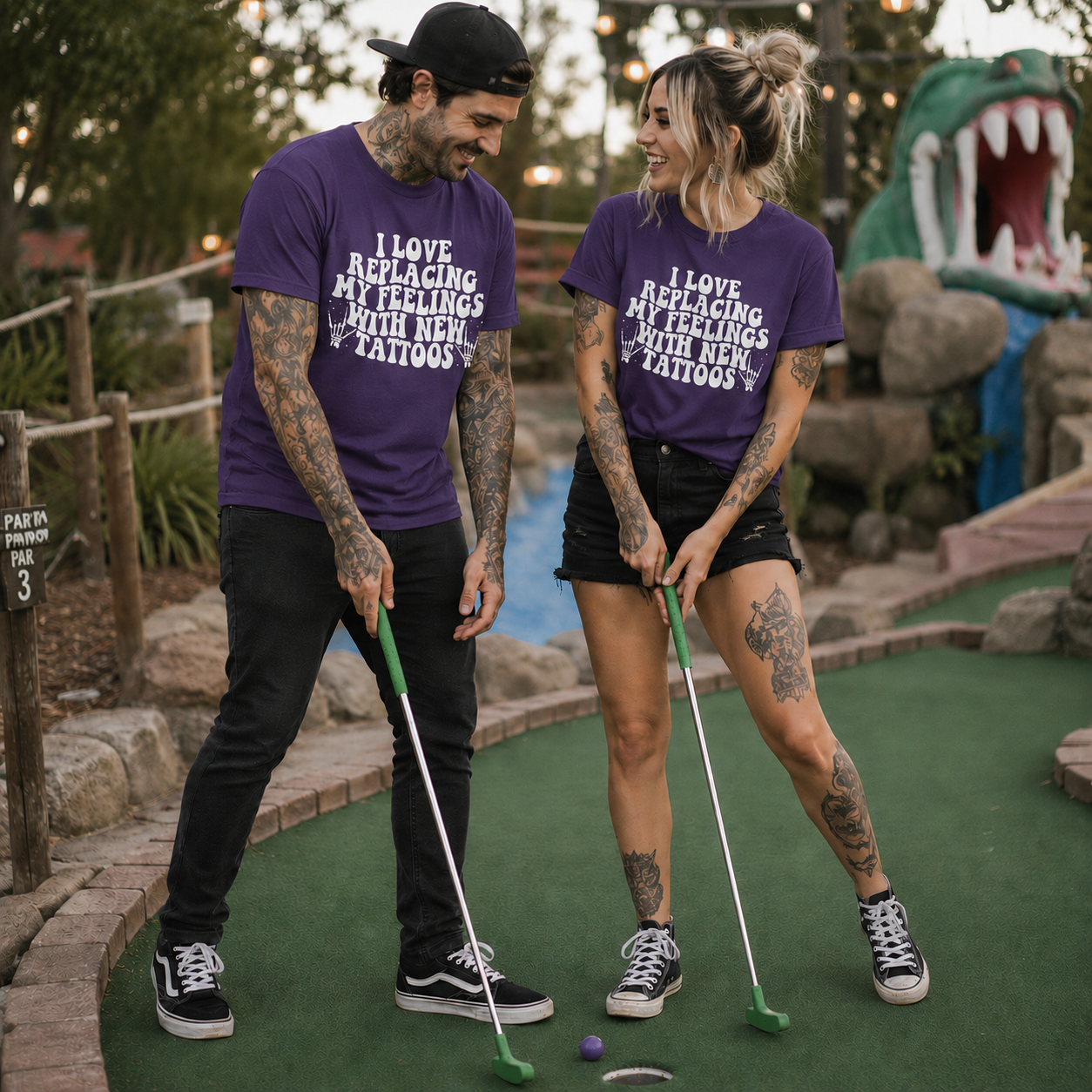 People wearing a heatherpurple colored  t-shirt with I love replacing my feelings with new tattoos white text design.