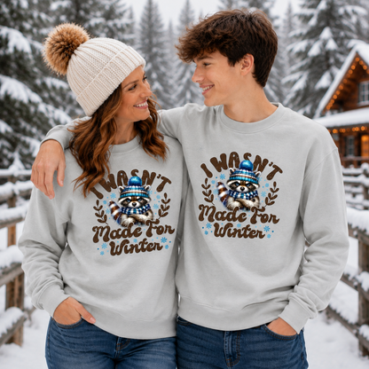 A mom and son wearing matching light gray sweatshirts with a winter-themed raccoon graphic and the text 'I WASN'T Made FOR Winter' in a snowy outdoor setting.