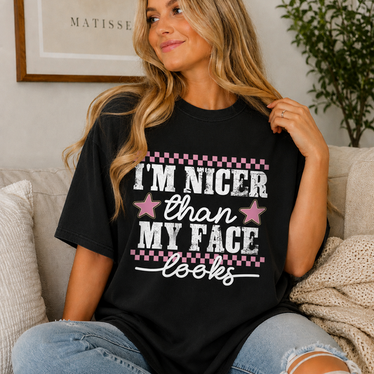 Woman with long blonde hair sitting on a couch wearing a black graphic t-shirt that says “I’m Nicer Than My Face Looks”