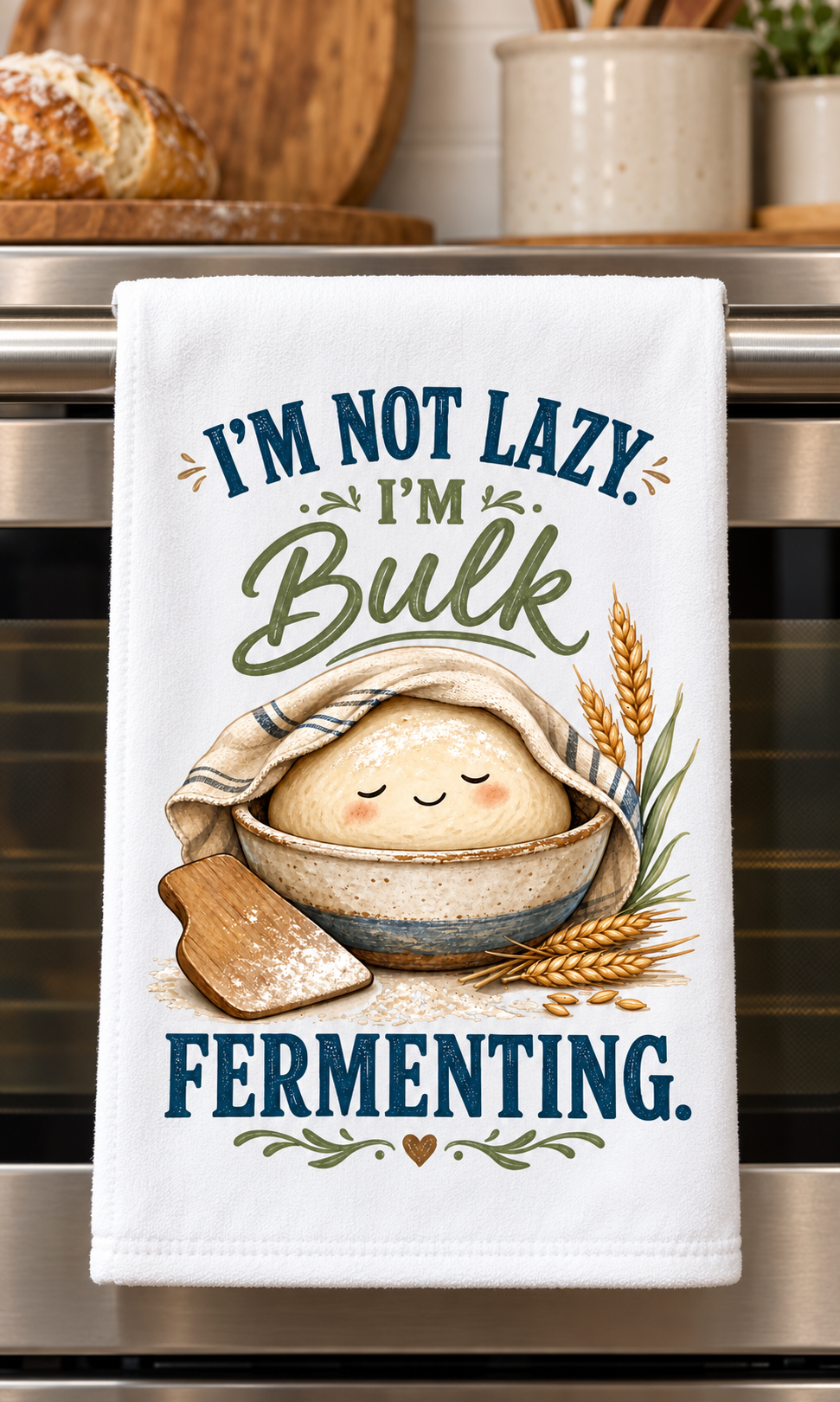 A white kitchen towel hanging on a stainless steel oven handle, printed with the humorous phrase 'I'M NOT LAZY. I'M Bulk FERMENTING.