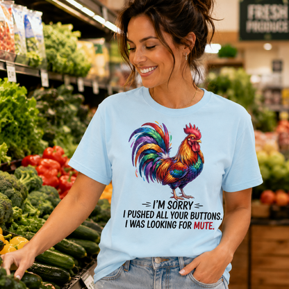 A woman in a grocery store aisle wearing a light blue graphic t-shirt with a colorful rooster and the text 'I'M SORRY I PUSHED ALL YOUR BUTTONS. I WAS LOOKING FOR MUTE.