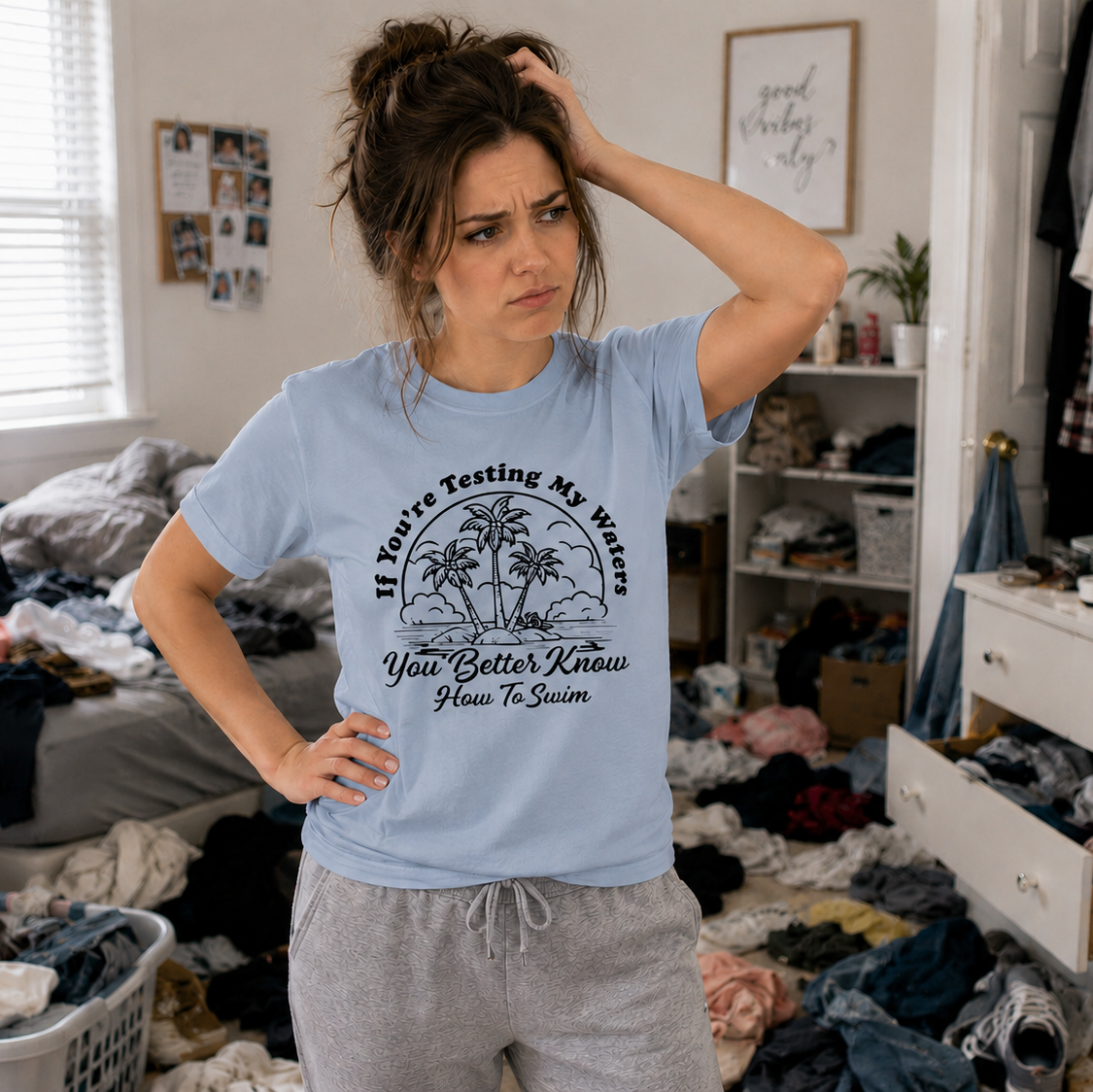 Woman in a messy room wearing a light blue t-shirt with text and graphics.